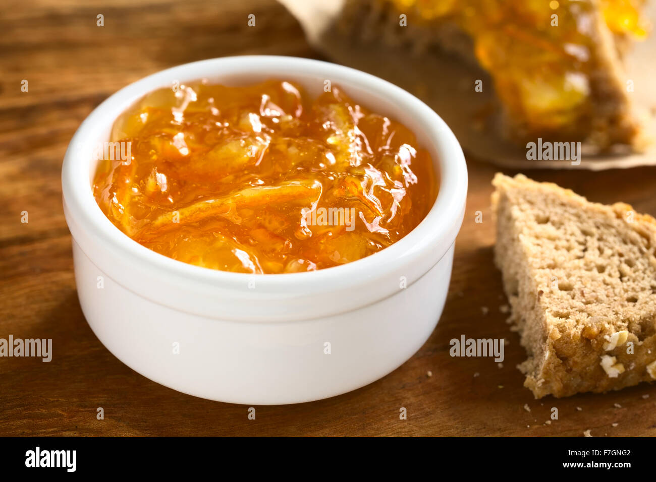 Marmellata di Arancia in una piccola ciotola di legno con pane sul lato, fotografati con luce naturale (messa a fuoco selettiva) Foto Stock