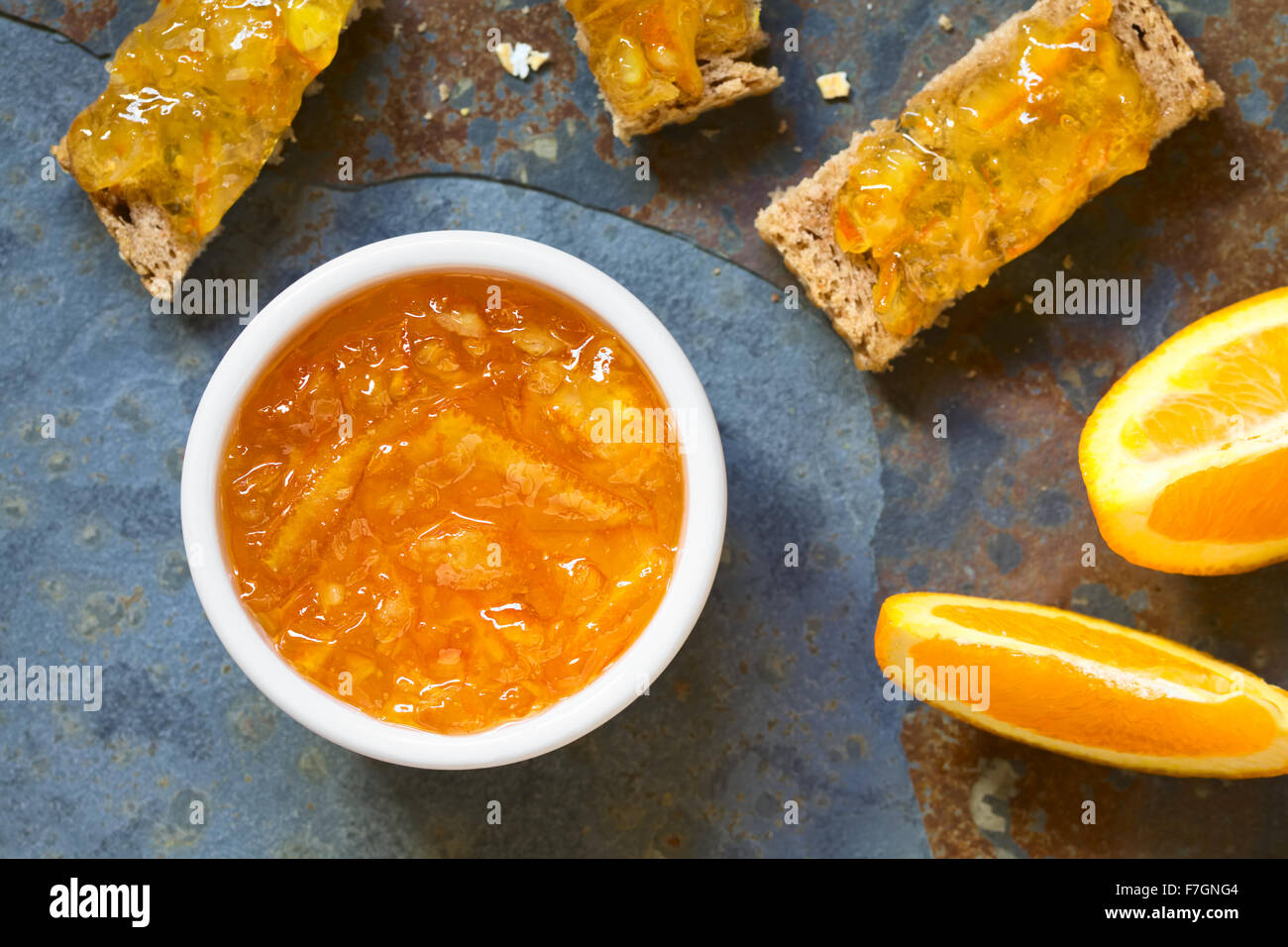 Marmellata di Arancia in una piccola ciotola con pane e spicchi d'arancia sul lato, fotografato overhead su ardesia con luce naturale Foto Stock