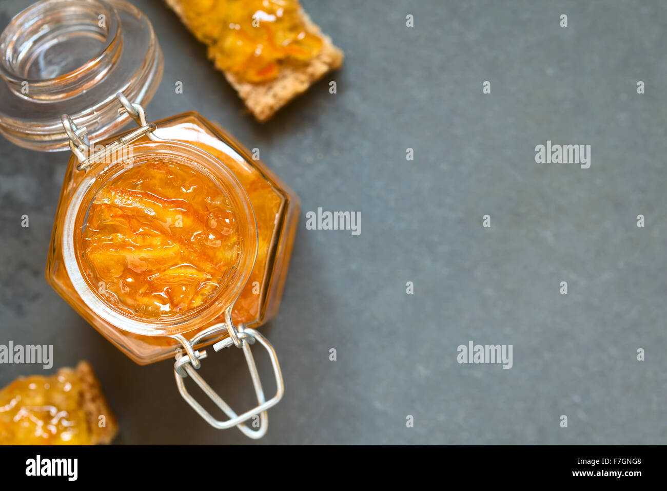 Orange jam swing-top jar, fette di pane con marmellata di arancione sul lato, fotografato overhead su ardesia con luce naturale Foto Stock