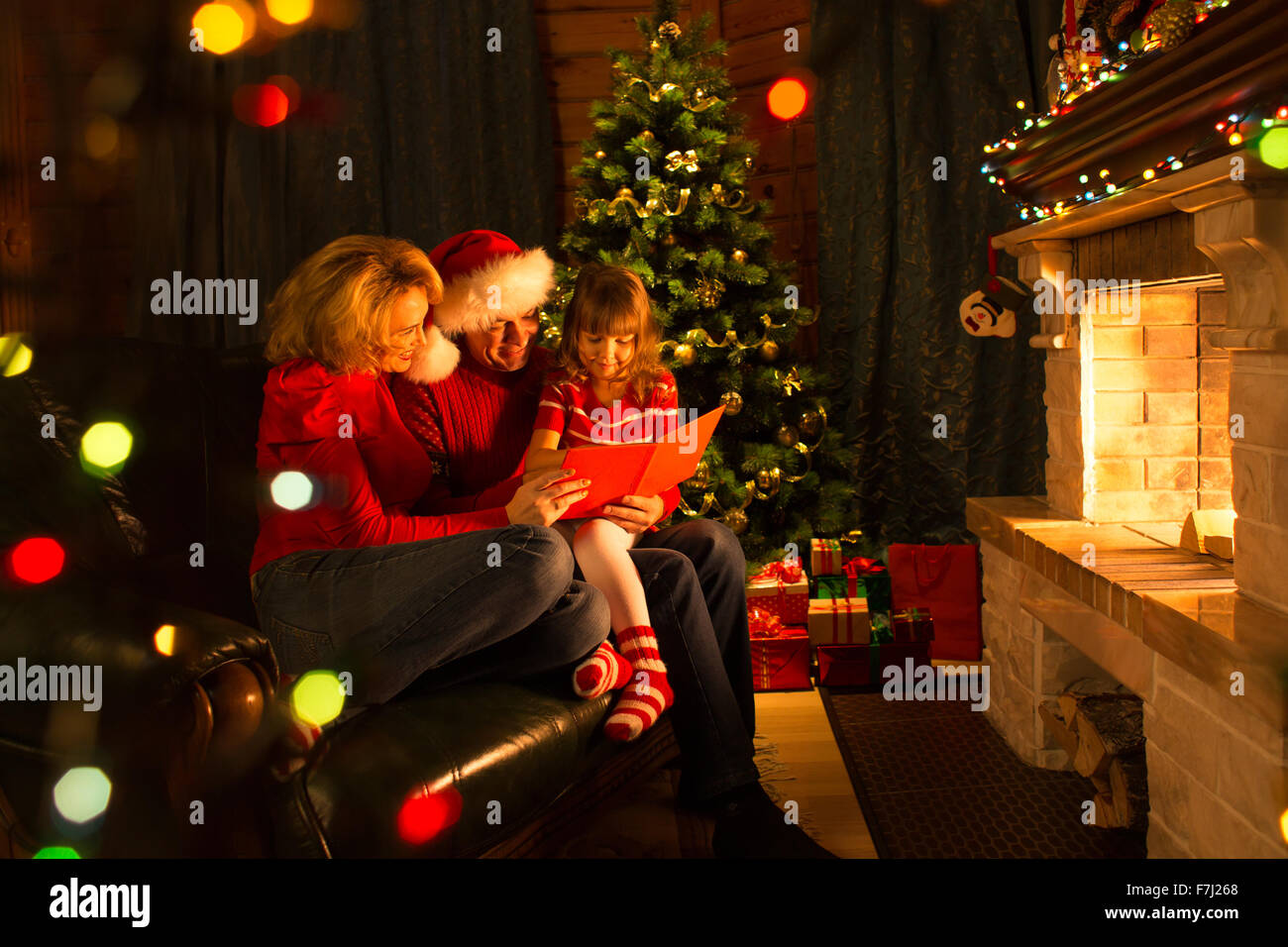 La famiglia felice Natale lettura libro seduti sul divano di fronte al caminetto nel salotto accogliente in inverno Foto Stock