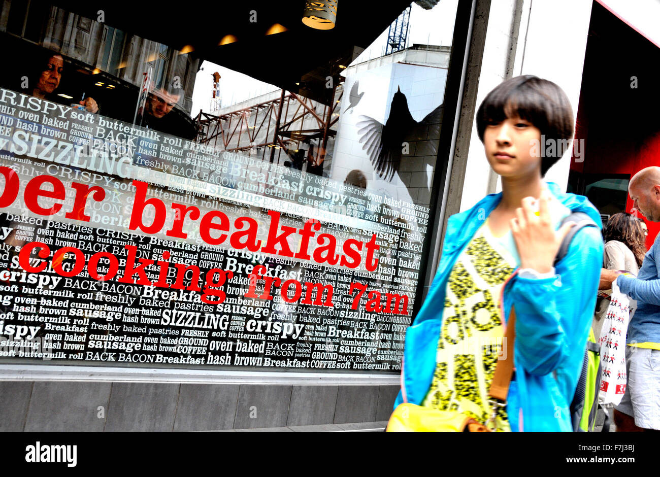Londra, Inghilterra, Regno Unito. La prima colazione - la giovane donna asiatica oltrepassando un cafe specializzato in b&b Foto Stock