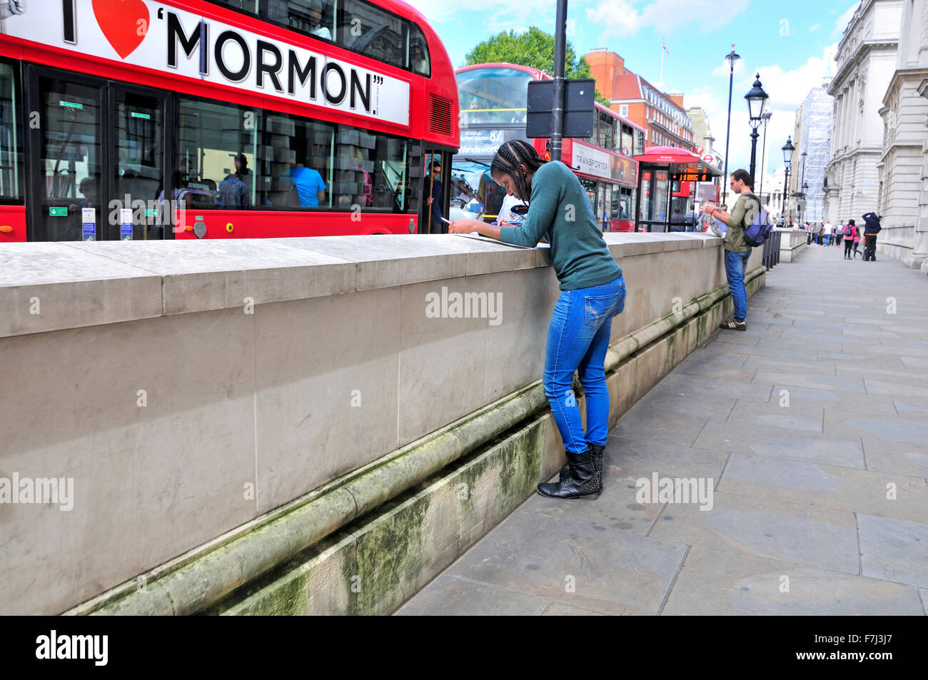 Londra, Inghilterra, Regno Unito. Giovane donna nera in Whithall guardando una mappa come un bus pubblicità 'Il Libro di Mormon' visualizza le unità passato Foto Stock