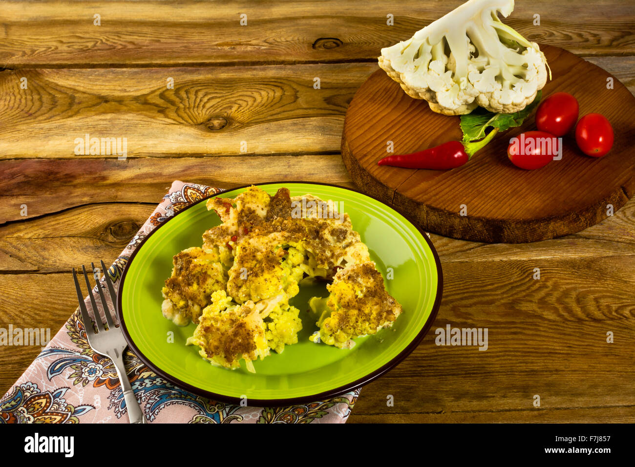 Cavolfiore al forno gratinati con formaggio su una piastra verde, rotonda di legno, pomodori, peperoni, orizzontale Foto Stock