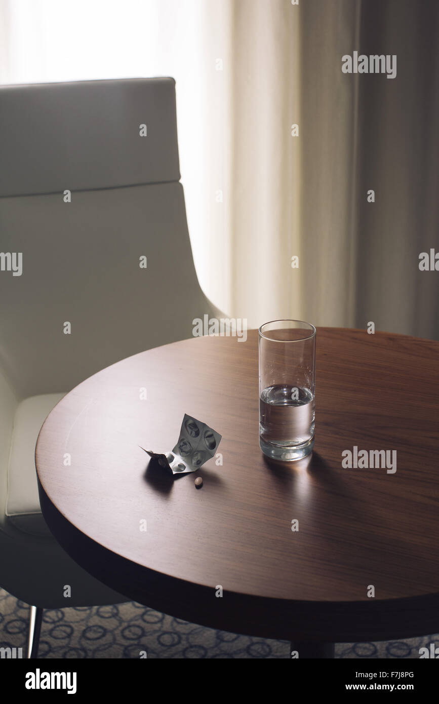 Bicchiere di acqua e medicinali sulla tavola in camera di albergo Foto Stock