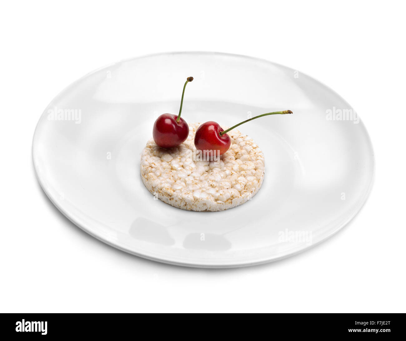 Ancora, "cibo sano" dieta. Due le ciliegie su torte di riso su un piatto di grandi dimensioni. Isolare il bianco. Foto Stock