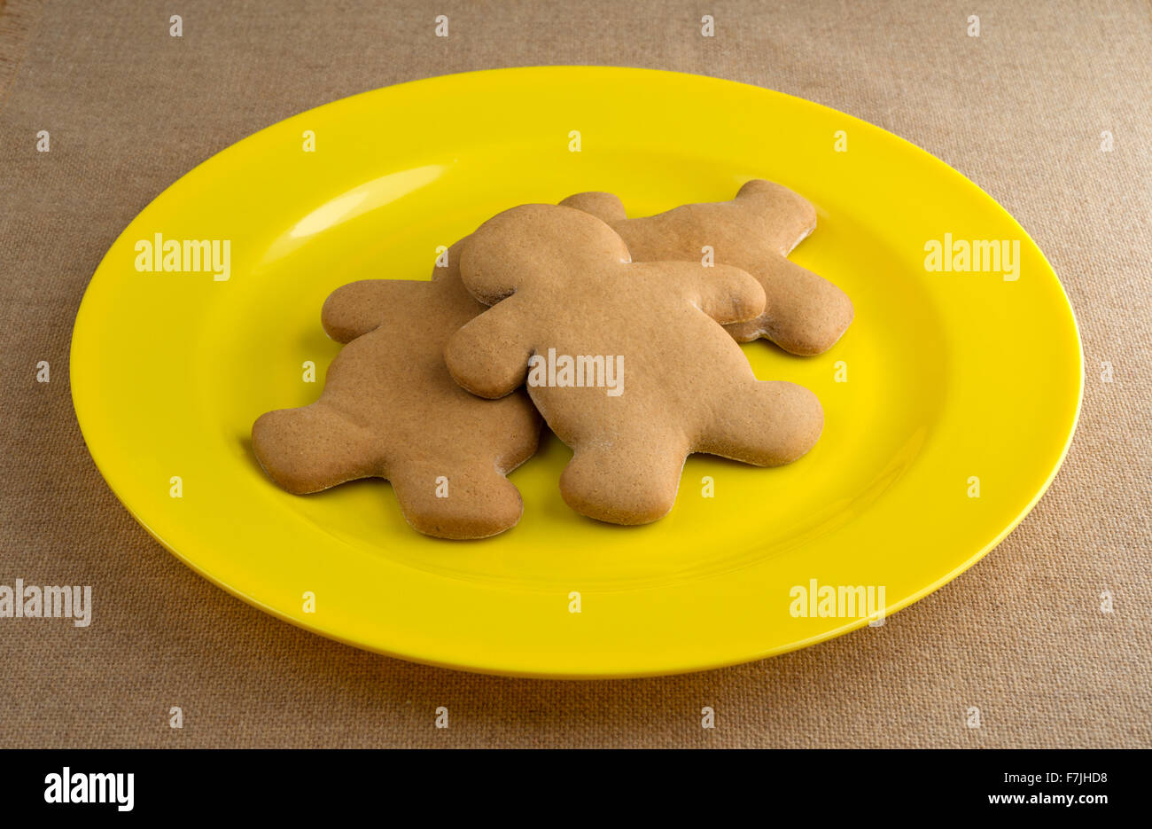 Tre appena sfornato gingerbread uomini su un grande plastico piastra gialla sulla cima di una tela stropicciata tovaglia illuminata con l naturale Foto Stock