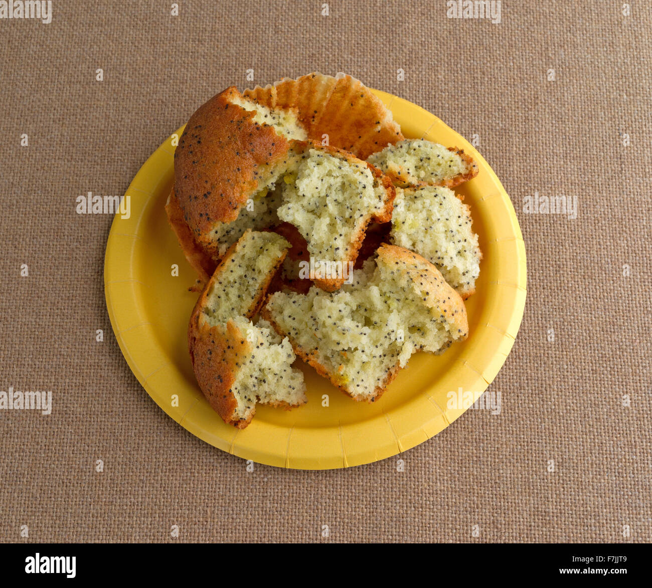 Un pane appena sfornato di pepe al limone muffin prima colazione che è stato rotto in più pezzi su una piastra di colore giallo sulla cima di una tovaglia di tela Foto Stock