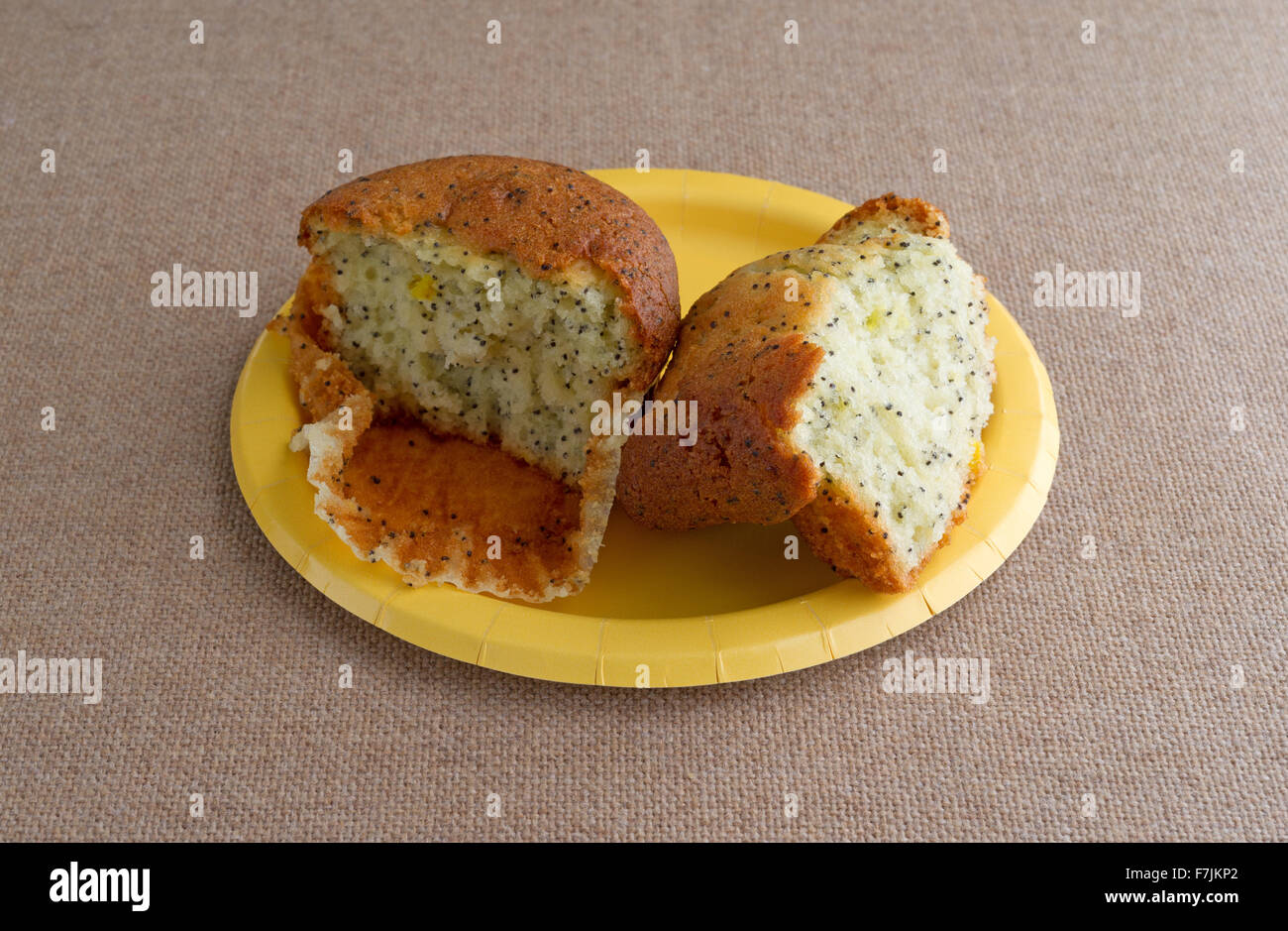 Un pane appena sfornato di pepe al limone muffin prima colazione che è stato rotto in metà su una piastra di colore giallo sulla cima di una tovaglia di tela si accende Foto Stock