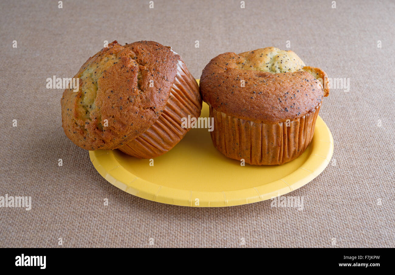 Una coppia di pane appena sfornato di pepe al limone colazione muffin su una piastra di colore giallo sulla cima di una tovaglia di tela illuminato con luce naturale Foto Stock
