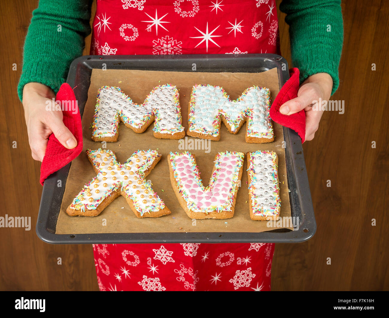 Donna che indossa il grembiule rosso azienda fatti in casa a base di pan di zenzero i cookie in forma di numeri romani in rappresentanza di 2016 Anno Nuovo data Foto Stock