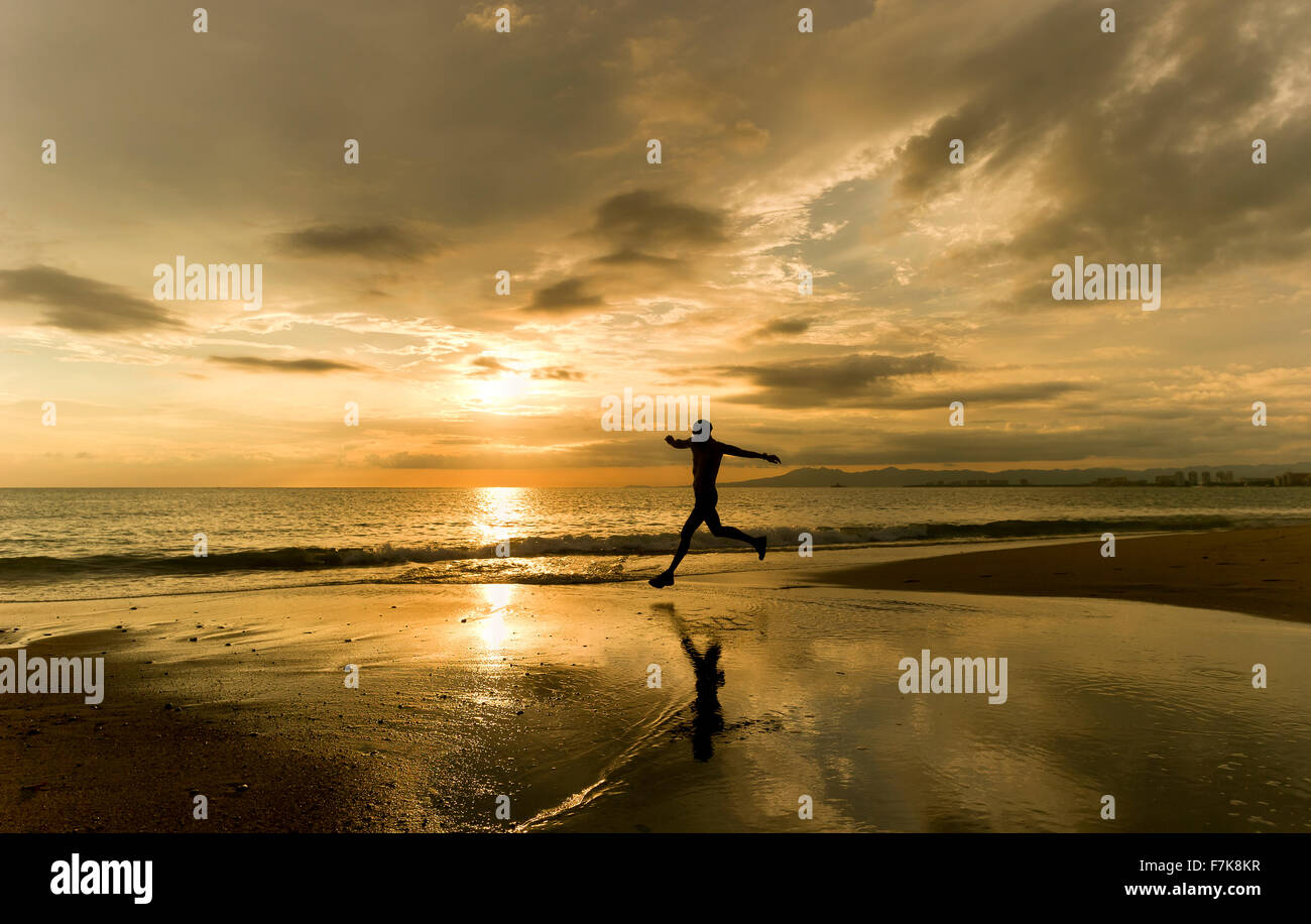 Runner silhouette è un uomo prendendo un balzo atletico con un oceano tramonto sullo sfondo mentre lungo la spiaggia. Foto Stock