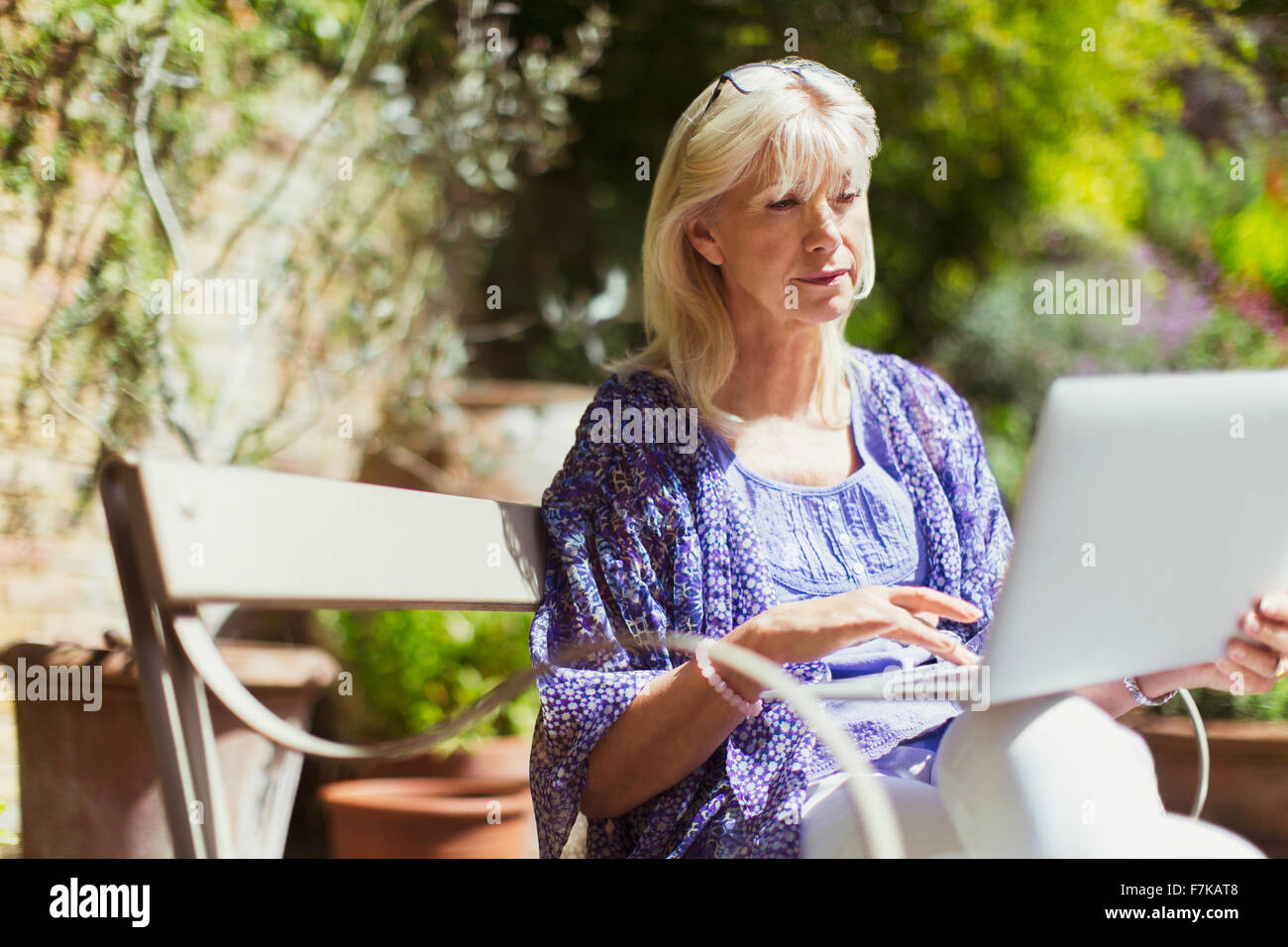 Senior donna utilizzando laptop sul soleggiato giardino panchina Foto Stock
