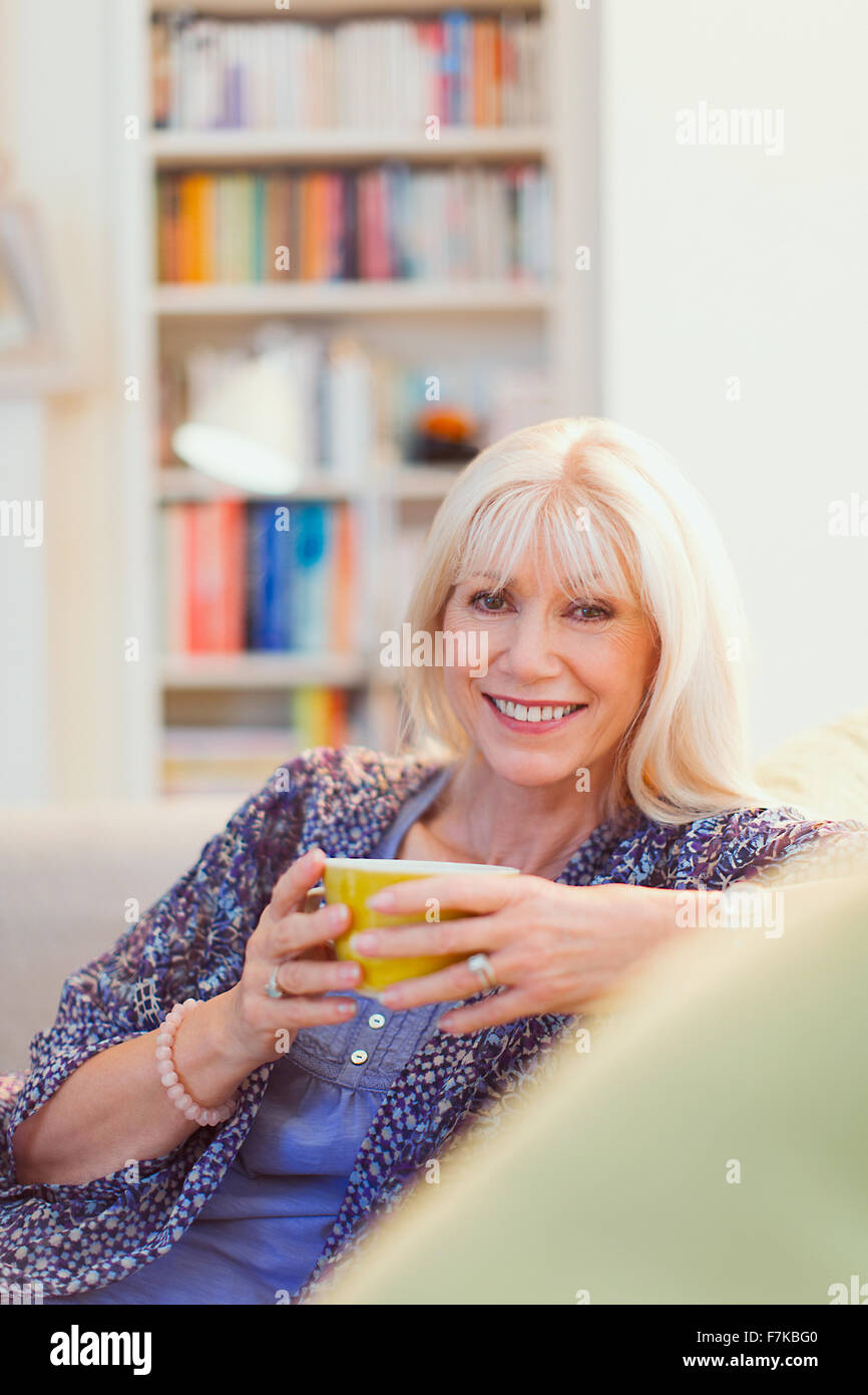 Ritratto sorridente donna senior di bere il caffè sul divano Foto Stock