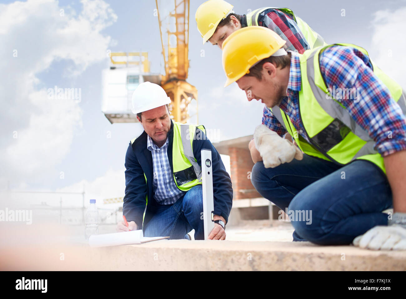 Lavoratori edili e ingegnere utilizzando lo strumento livello al sito in costruzione Foto Stock