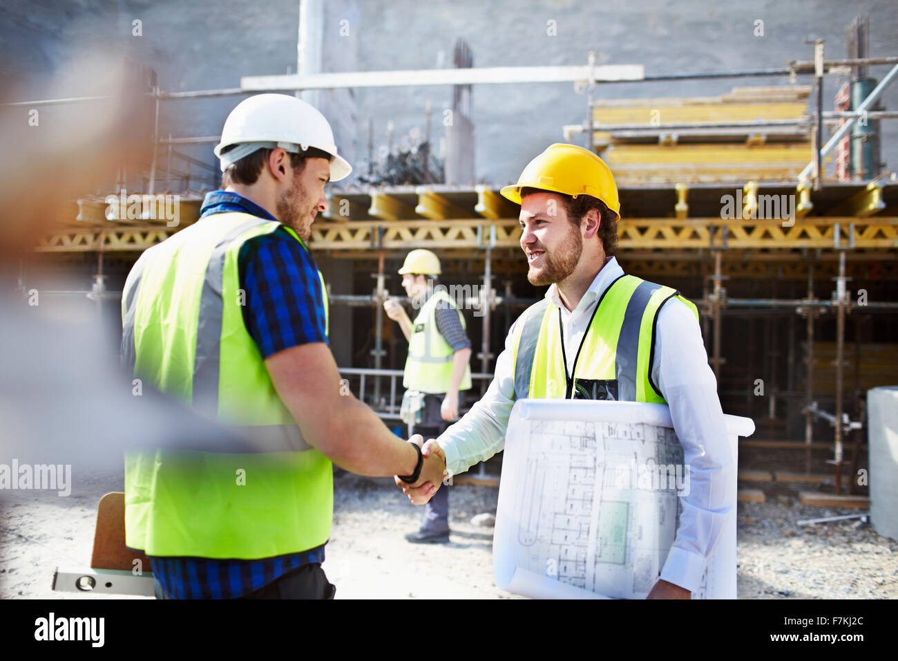 Lavoratore edile e ingegnere con blueprint handshaking al sito in costruzione Foto Stock