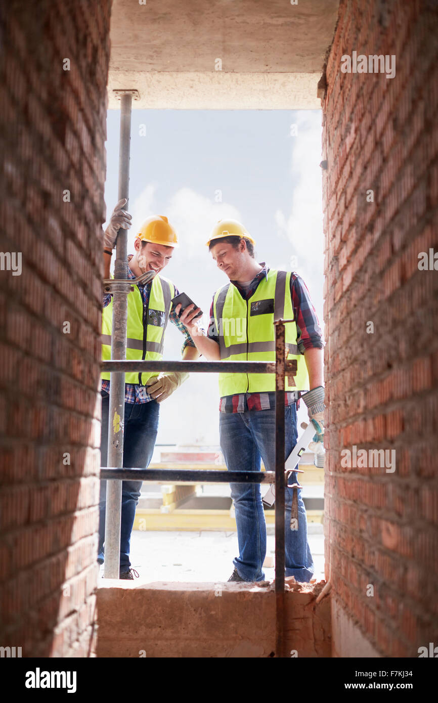 Lavoratori edili texting con un telefono cellulare al sito in costruzione Foto Stock