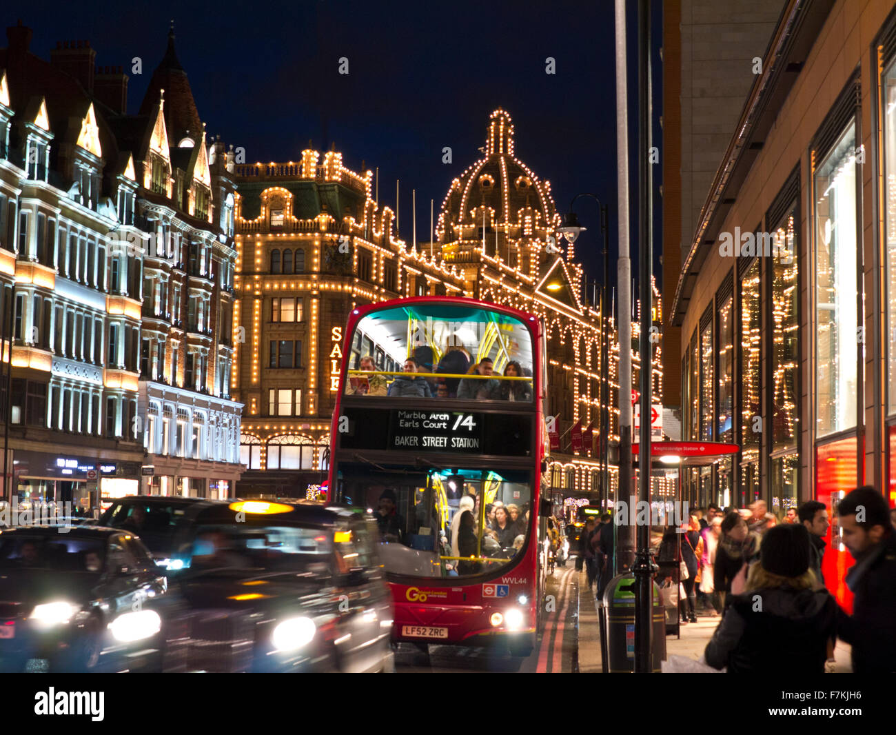 TAXI TRAFFICO DI NATALE ULEZ SHOPPERS Harrods grande magazzino di notte con il segno 'sale' illuminato shoppers rosso autobus, traffico trafficato Knightsbridge Londra SW1 Foto Stock