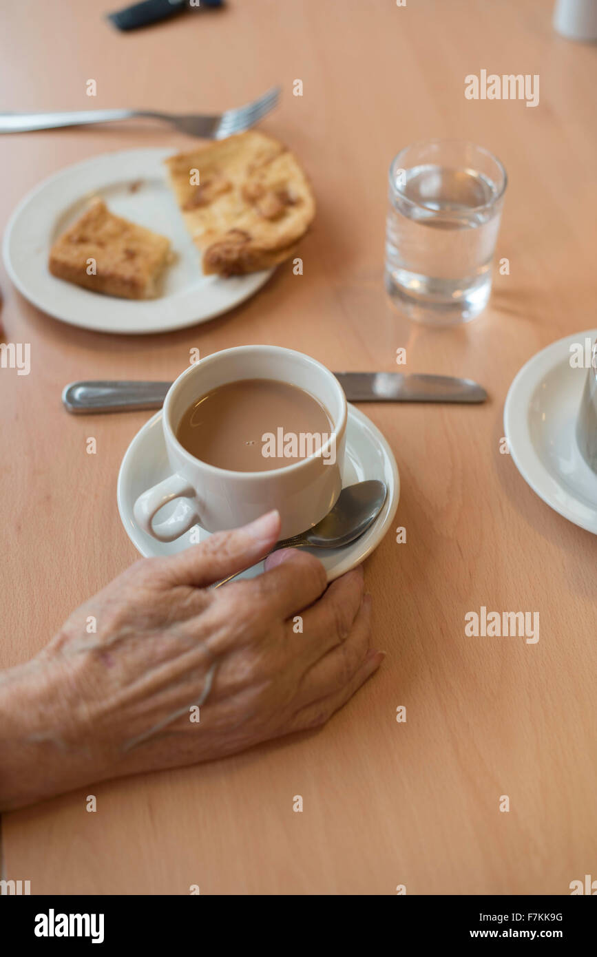 Un anziano mano con una tazza di tè e una fetta di pane tostato in un vecchio folks home Foto Stock