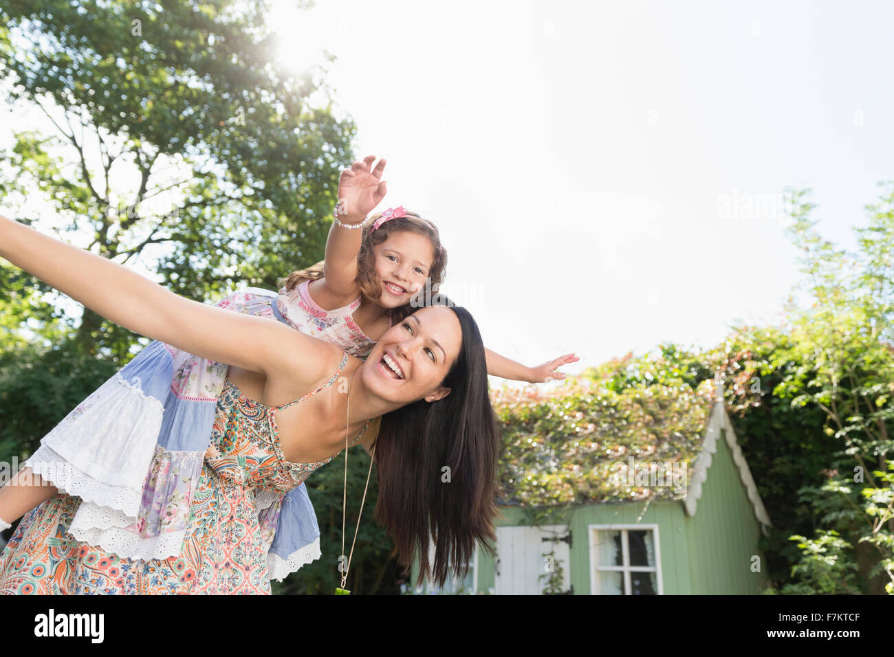 Carefree madre piggybacking figlia con le braccia aperte in cortile Foto Stock