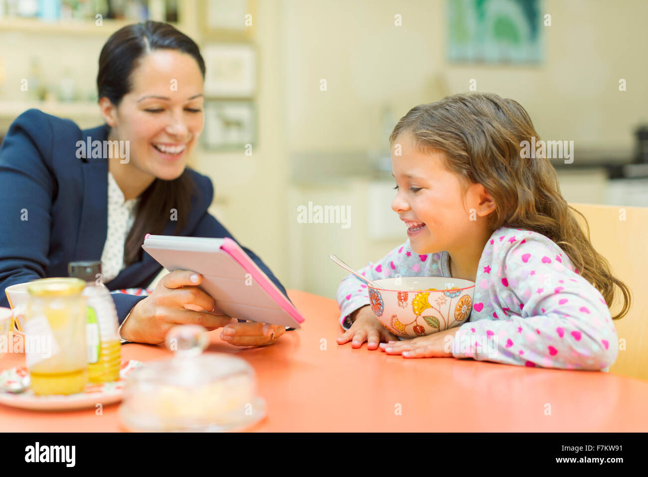 Madre e figlia utilizzando digitale compressa al tavolo per la colazione Foto Stock