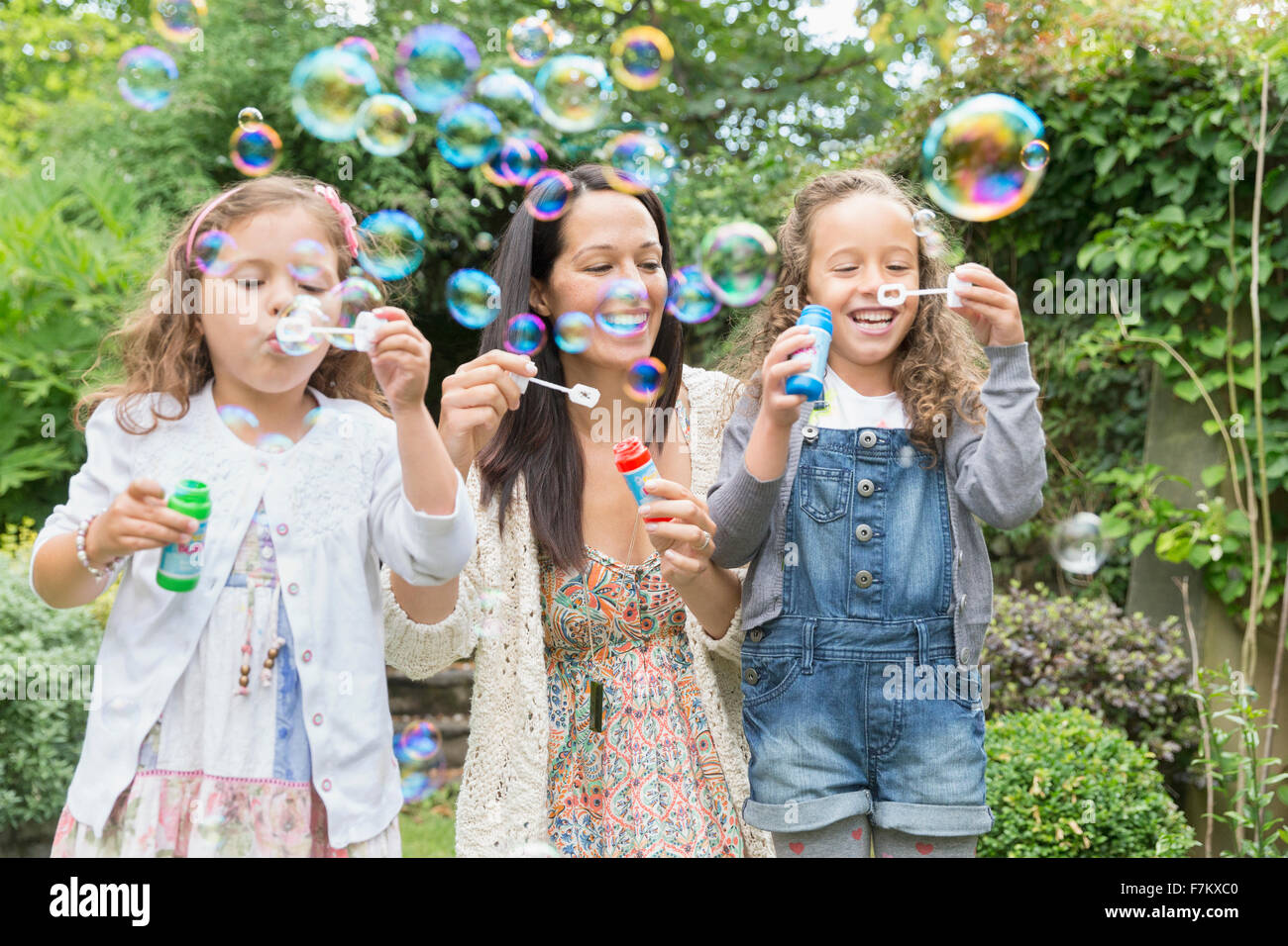 La madre e le figlie a soffiare bolle nel cortile posteriore Foto Stock