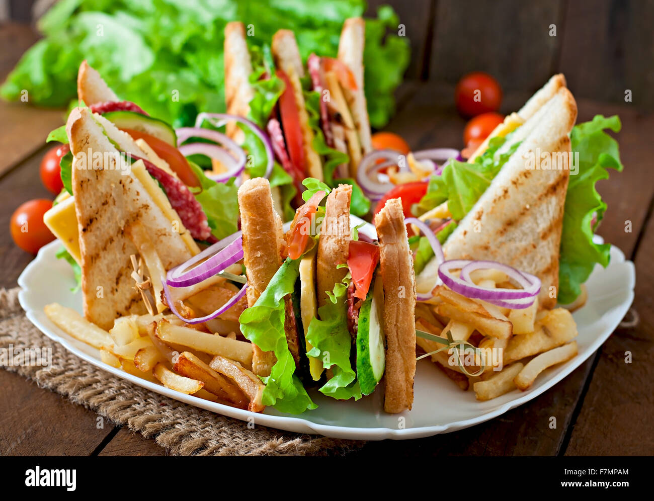 Club sandwich con formaggio, cetriolo, pomodoro, carne affumicata e salame. Servito con patate fritte. Foto Stock