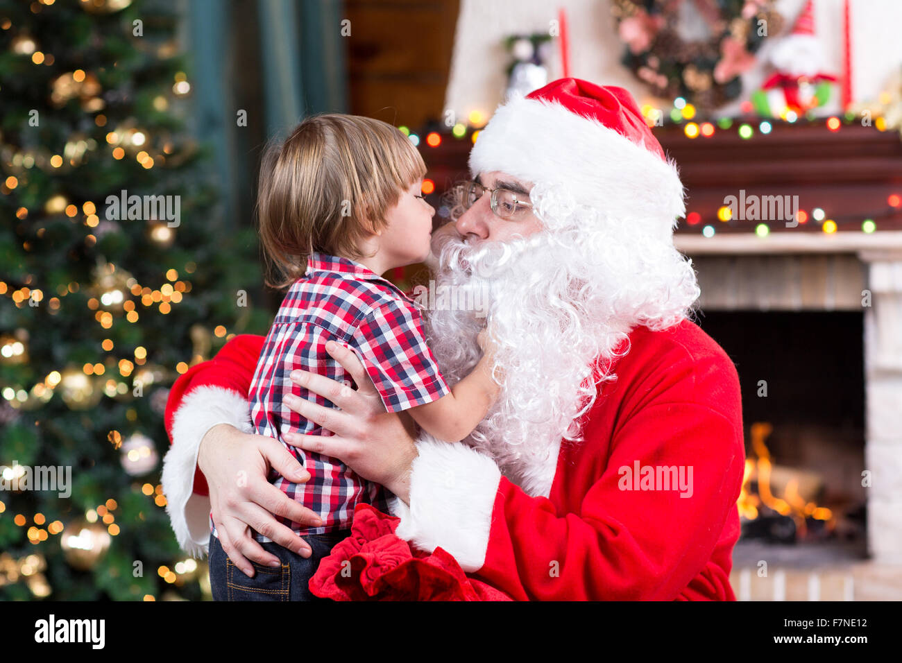 Bambino toddler boy kissing Santa Claus seduta vicino ad albero di Natale Foto Stock