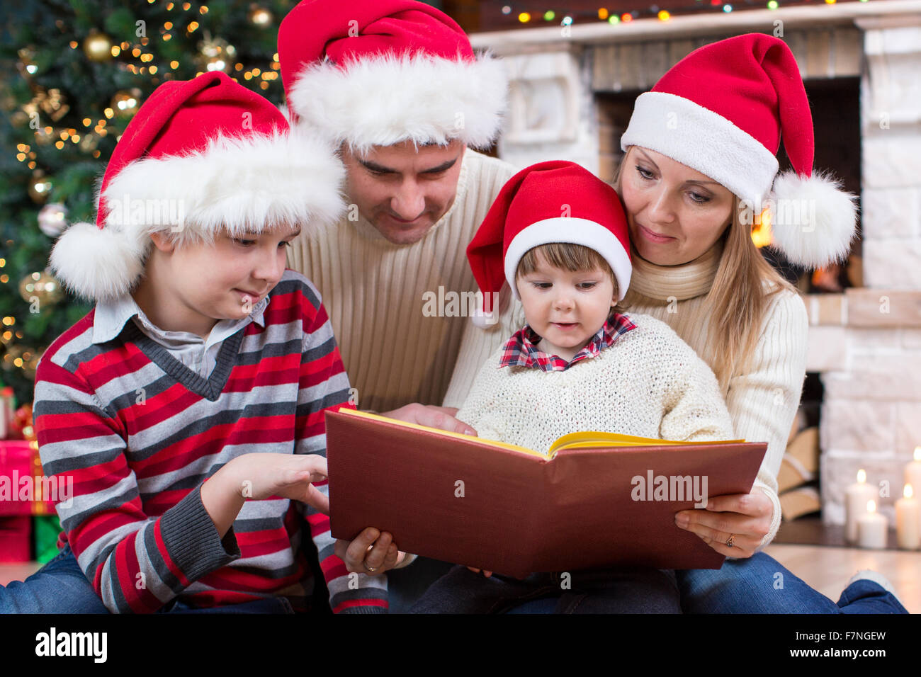 Famiglia leggendo un libro nella parte anteriore dell albero di Natale Foto Stock