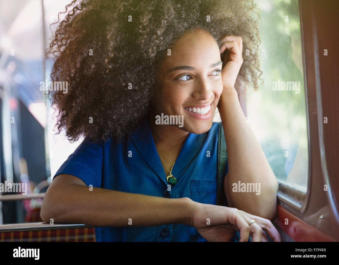 Donna sorridente con afro bus di equitazione a guardare fuori dalla finestra Foto Stock