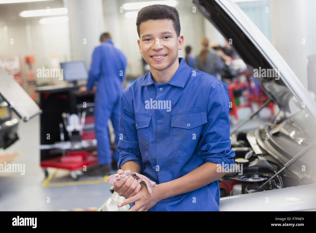 Ritratto meccanico sorridente appoggiato su auto nel negozio di riparazioni auto Foto Stock