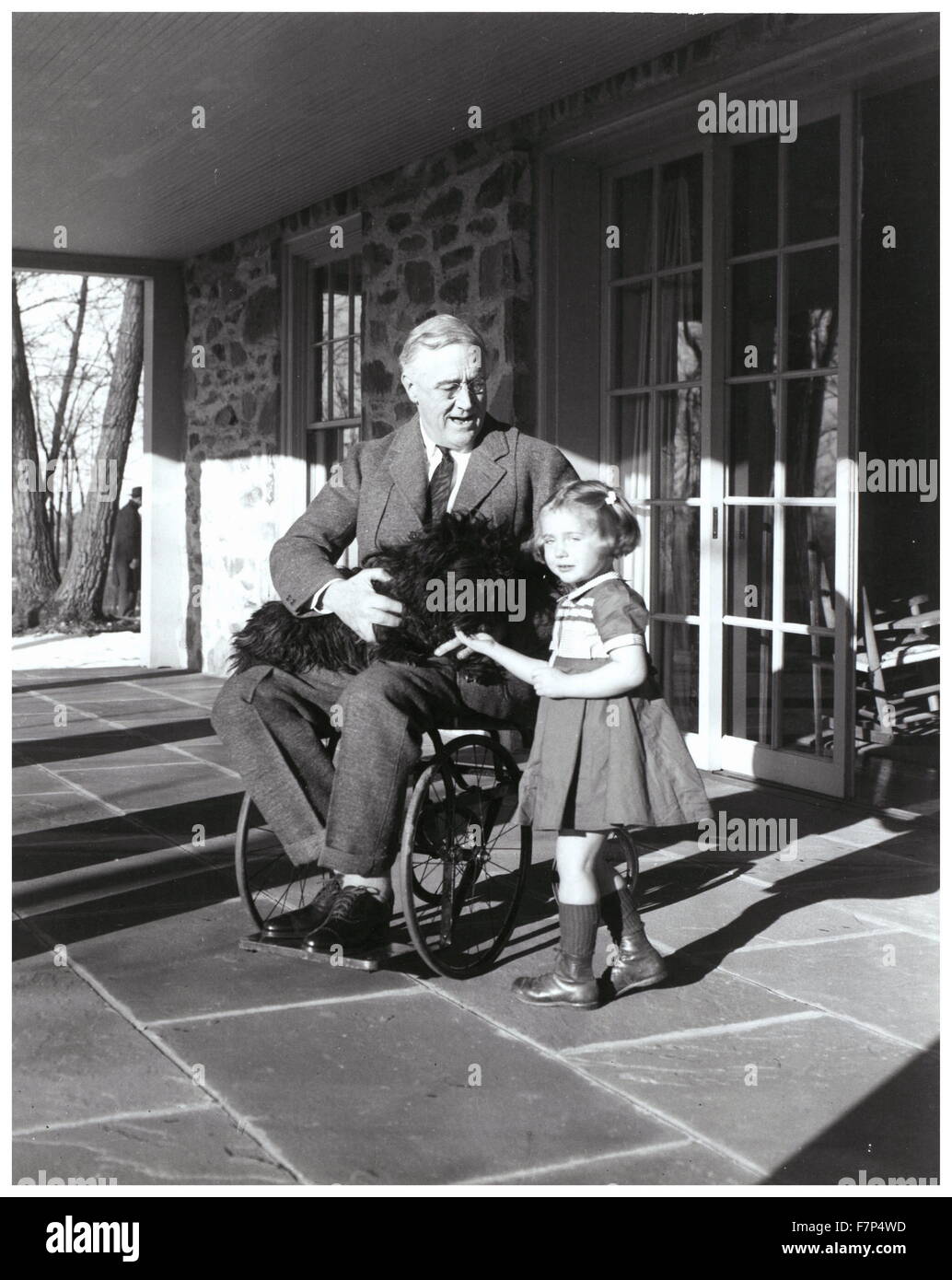 Il presidente statunitense Franklin Roosevelt tiene il suo cane come egli siede su di una terrazza con Ruthie Bie;la figlia di un membro del personale 1938 Foto Stock