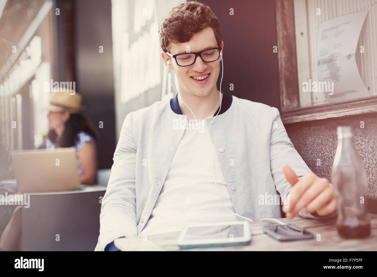 Sorridente giovane uomo ascoltare musica con le cuffie e il lettore mp3 al cafè sul marciapiede Foto Stock