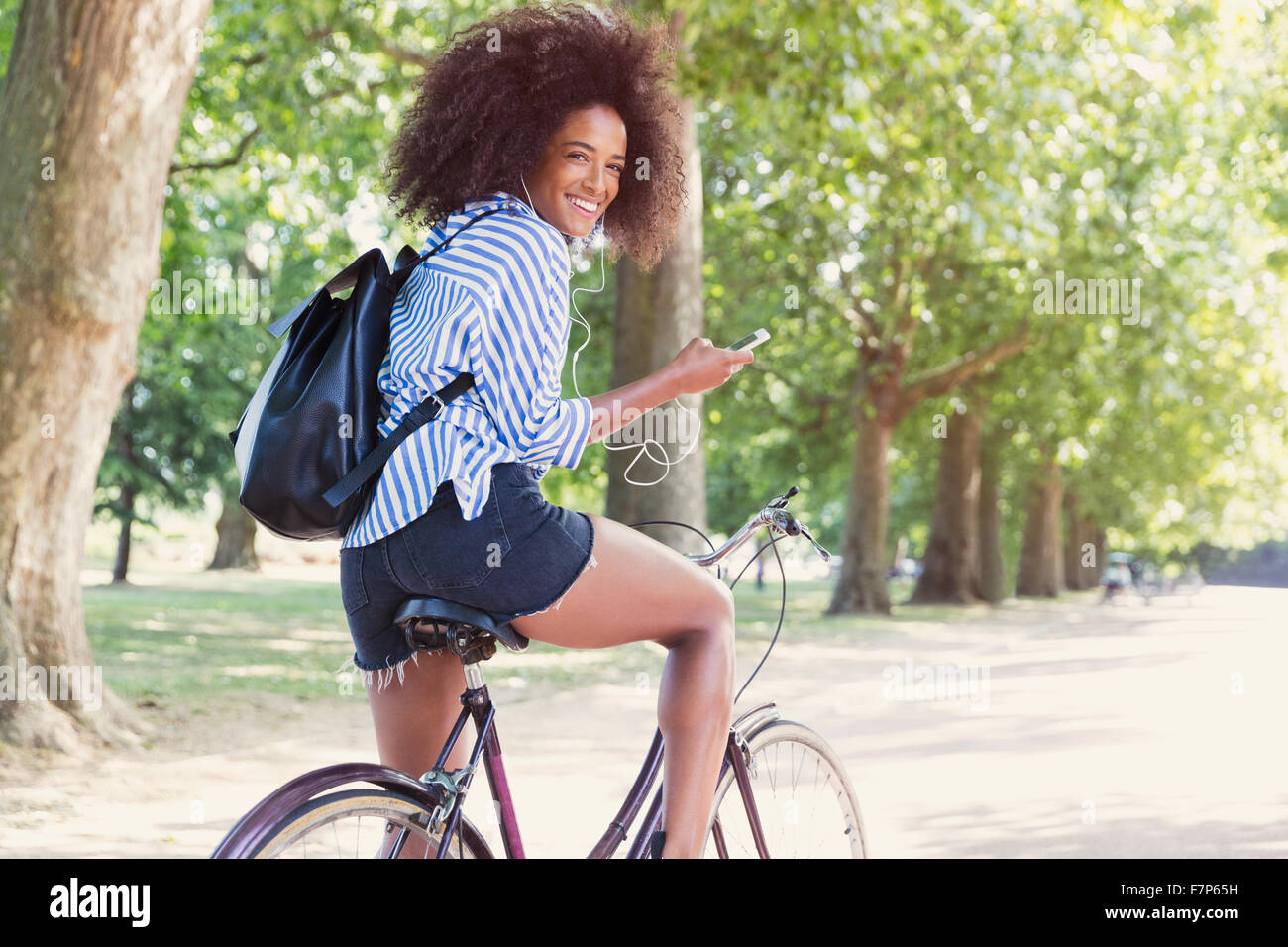 Ritratto di donna sorridente Bicicletta Equitazione con lettore mp3 e le cuffie in posizione di parcheggio Foto Stock