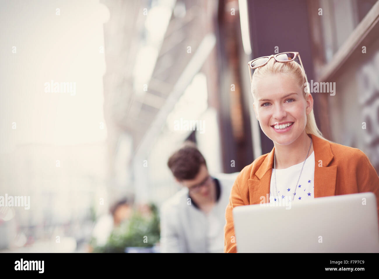 Ritratto sorridente donna bionda con computer portatile presso cafè sul marciapiede Foto Stock