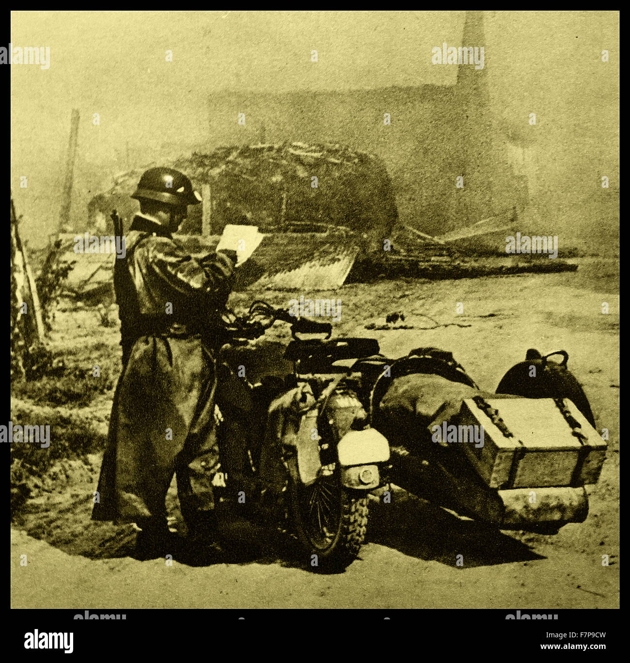 Soldato tedesco sorge accanto ad una moto, al di fuori di un paese devastato in Francia. Prese durante l'invasione della Francia 1940. Foto Stock
