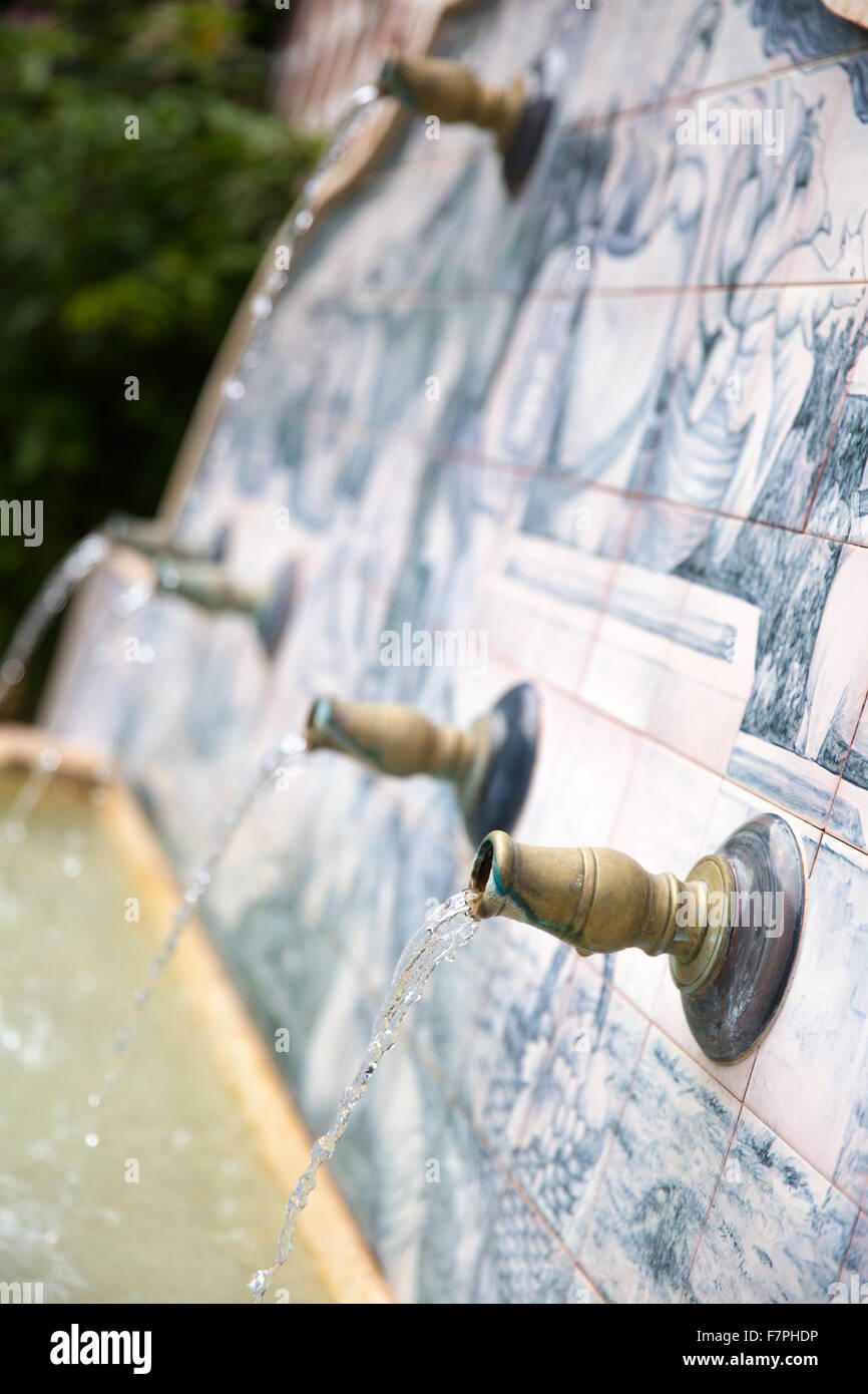 Flussi di acqua che esce di alcuni tubi metallici in una fontana del paese fatti a mano con disegni di ceramica Foto Stock