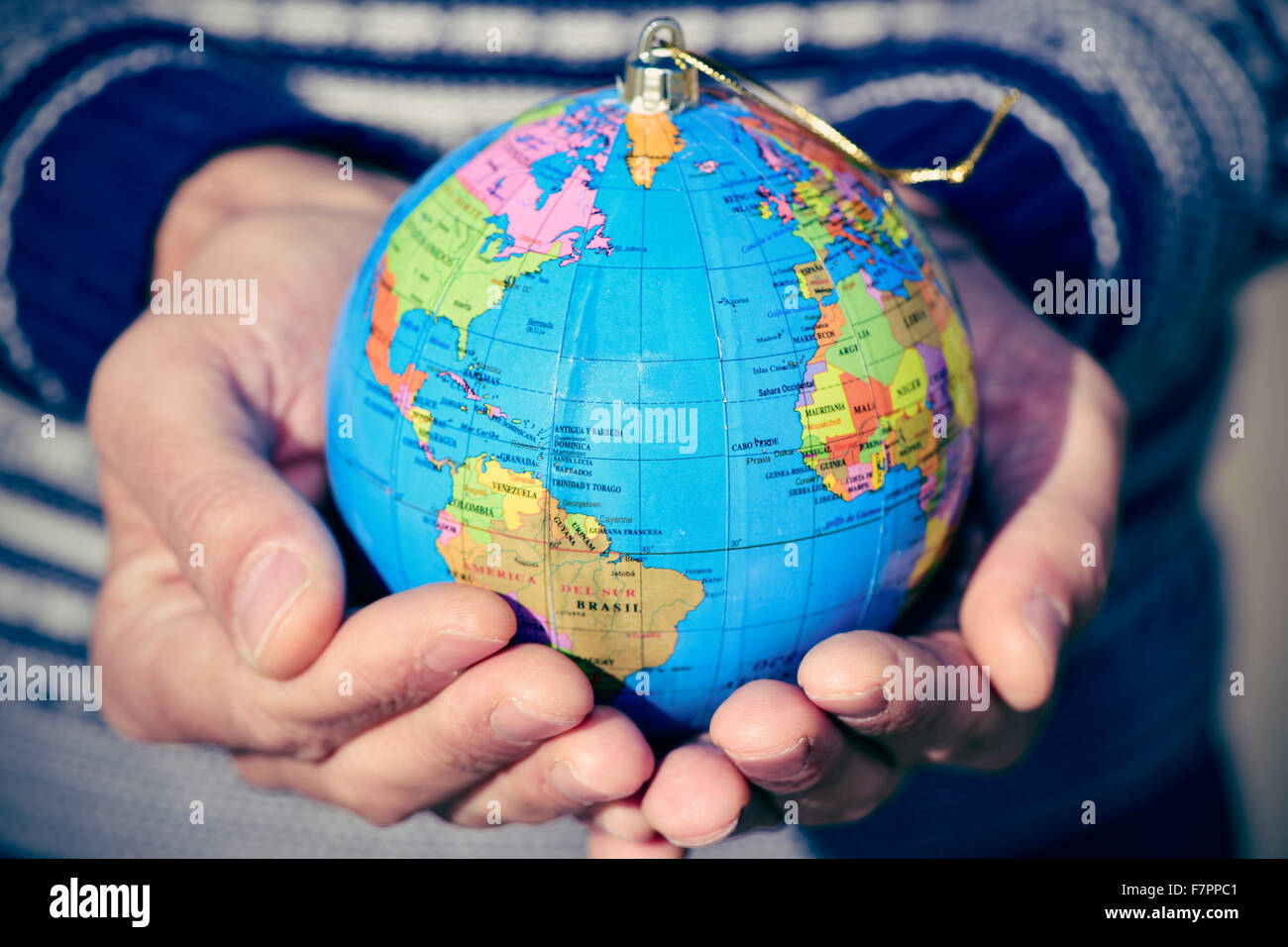 Primo piano di un giovane uomo caucasico con un mondo globo con una golden stringa come una palla di Natale nelle sue mani Foto Stock