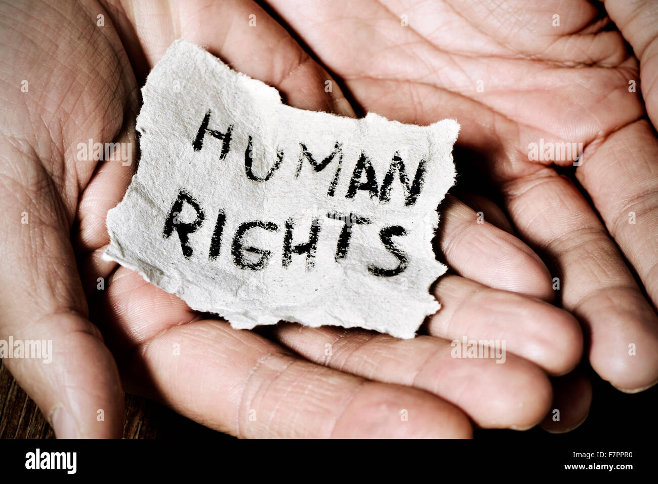Primo piano delle mani di un giovane con un pezzo di carta con il testo dei diritti umani scritta in esso, con un effetto drammatico Foto Stock