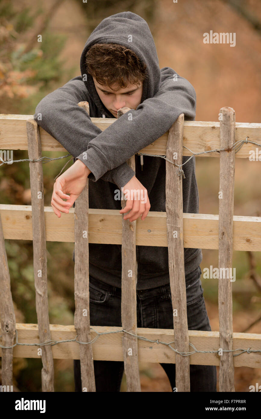 Triste ragazzo adolescente appoggiato su di una recinzione Foto Stock