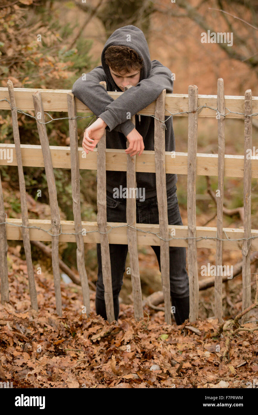 Triste ragazzo adolescente appoggiato su di una recinzione Foto Stock