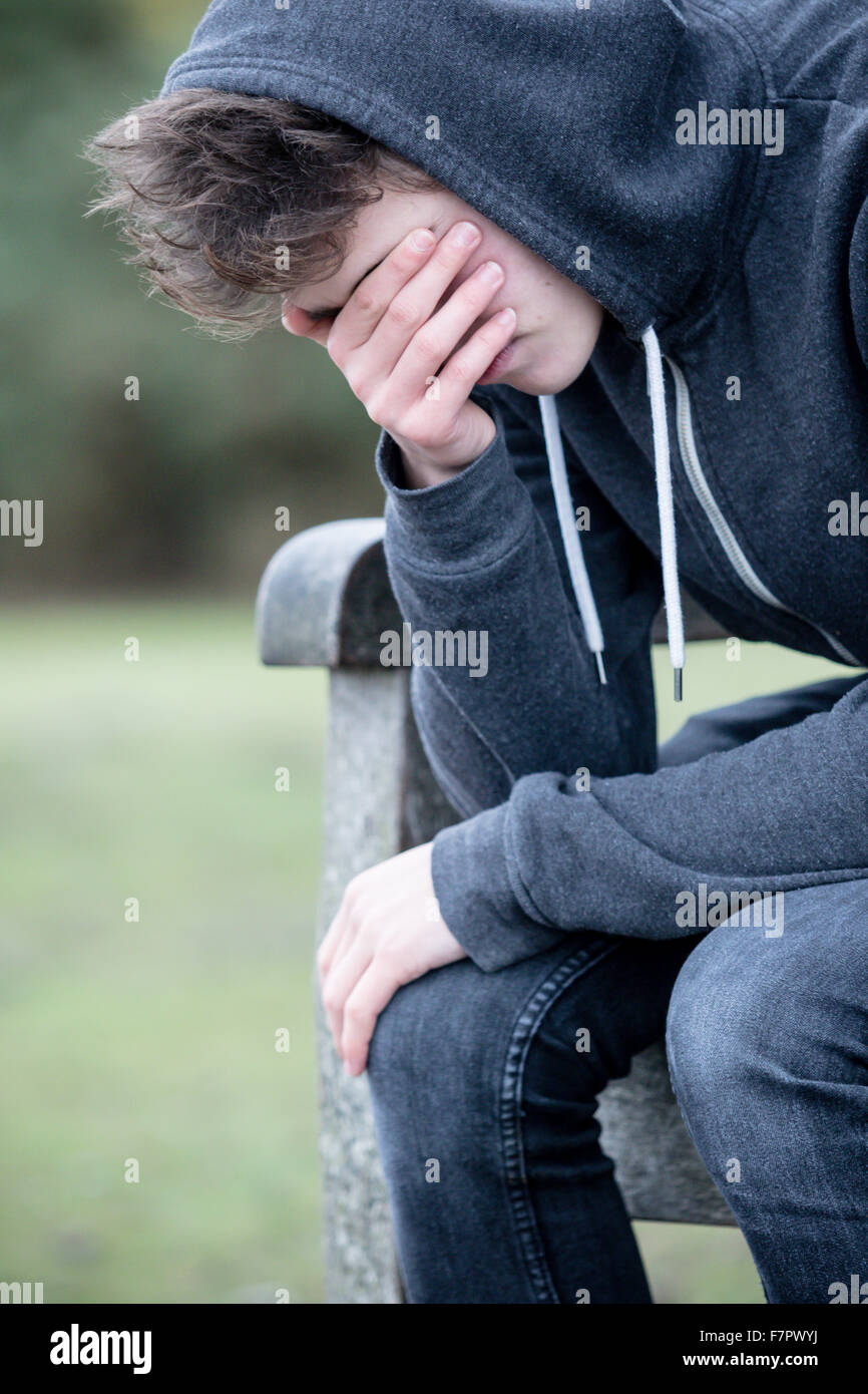 Triste ragazzo adolescente seduto su una panchina nel parco Foto Stock