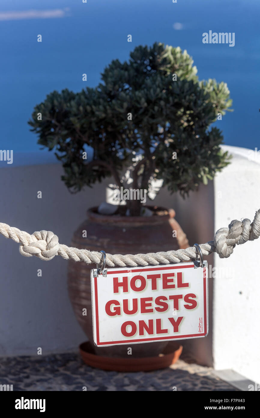Insegna "SOLO OSPITI DELL'HOTEL" su una barriera di corda di fronte a una terrazza privata che si affaccia sul Mar Egeo a Oia, Santorini, Grecia. Concetto di sovraturismo Foto Stock