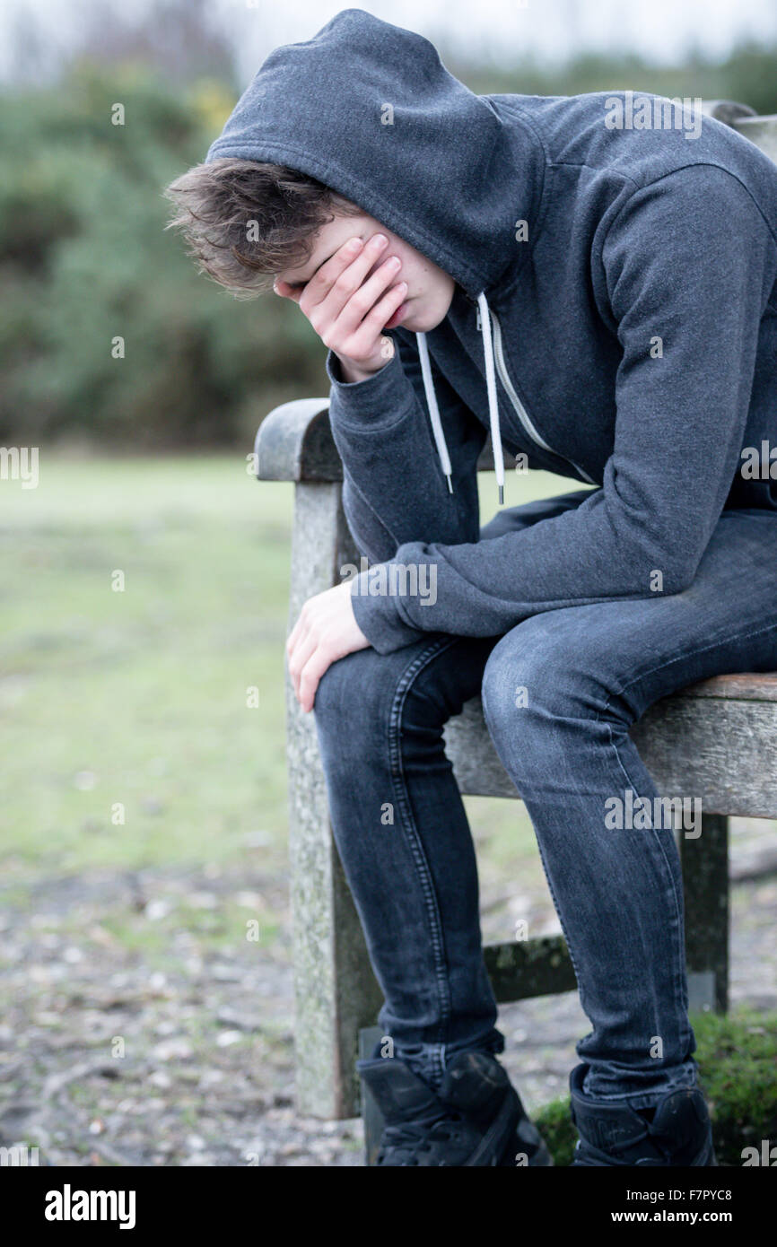 Triste ragazzo adolescente seduto su una panchina nel parco Foto Stock