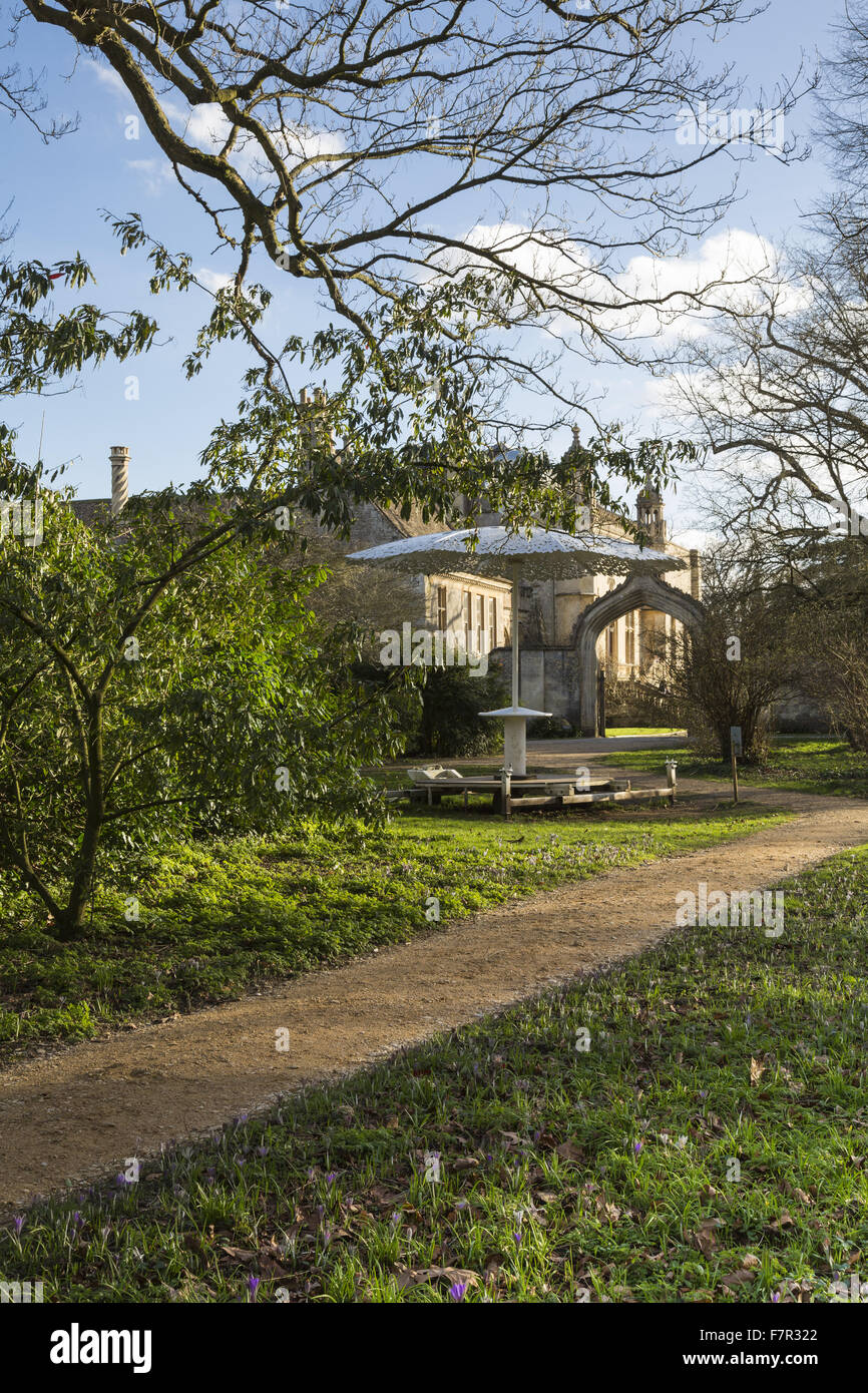 Vista della facciata ovest di Lacock Abbey, Wiltshire, visto da boschi, con bucaneve e crochi in fiore lungo un percorso. Foto Stock
