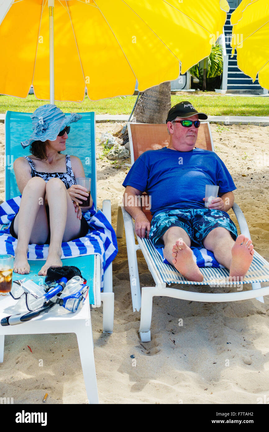 A 50 anni coppia caucasica in rilassanti sedie a sdraio sotto gli ombrelloni sulla spiaggia di St. Croix, U.S. Isole Vergini. USVI, U.S.V.I. Foto Stock