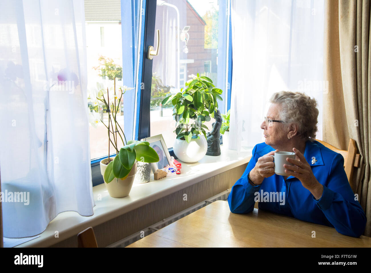 La nonna di bere il caffè e guardare fuori la sua finestra in casa di riposo per anziani Foto Stock