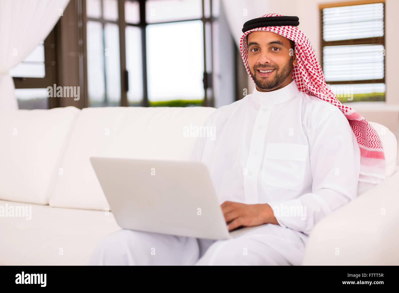Buona ricerca uomo islamico utilizzando laptop in salotto Foto Stock