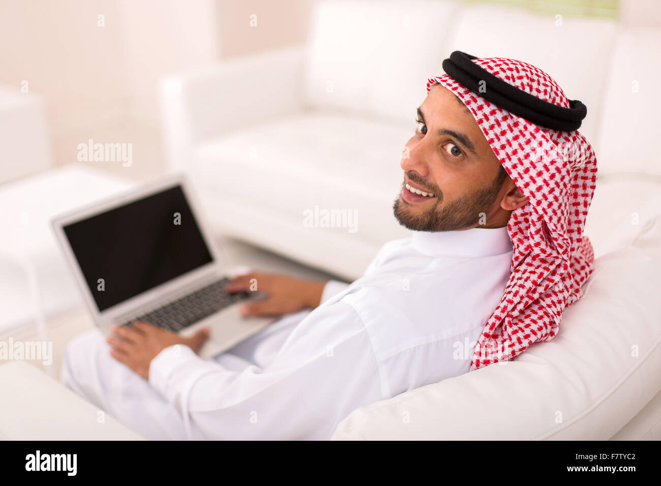 Felice giovane uomo arabo con laptop guardando indietro Foto Stock