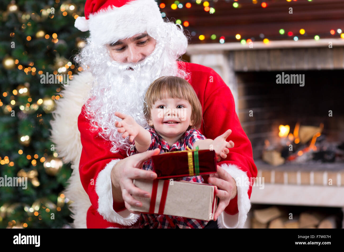 Il Natale e il concetto di infanzia - bambino sorridente ragazzo con Babbo Natale e regali su sfondo luci Foto Stock