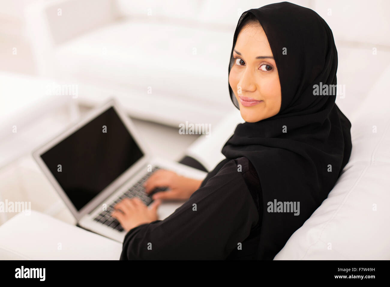 Attraente donna musulmana con computer portatile a casa Foto Stock